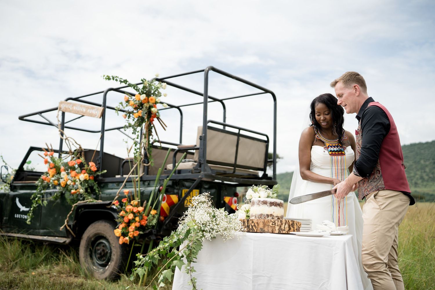 Wedding reception setup with decorated safari vehicle and refreshment table in African savanna.