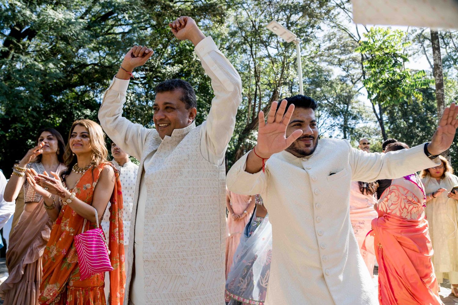 Outdoor wedding celebration with guests dancing in traditional white and colorful attire.