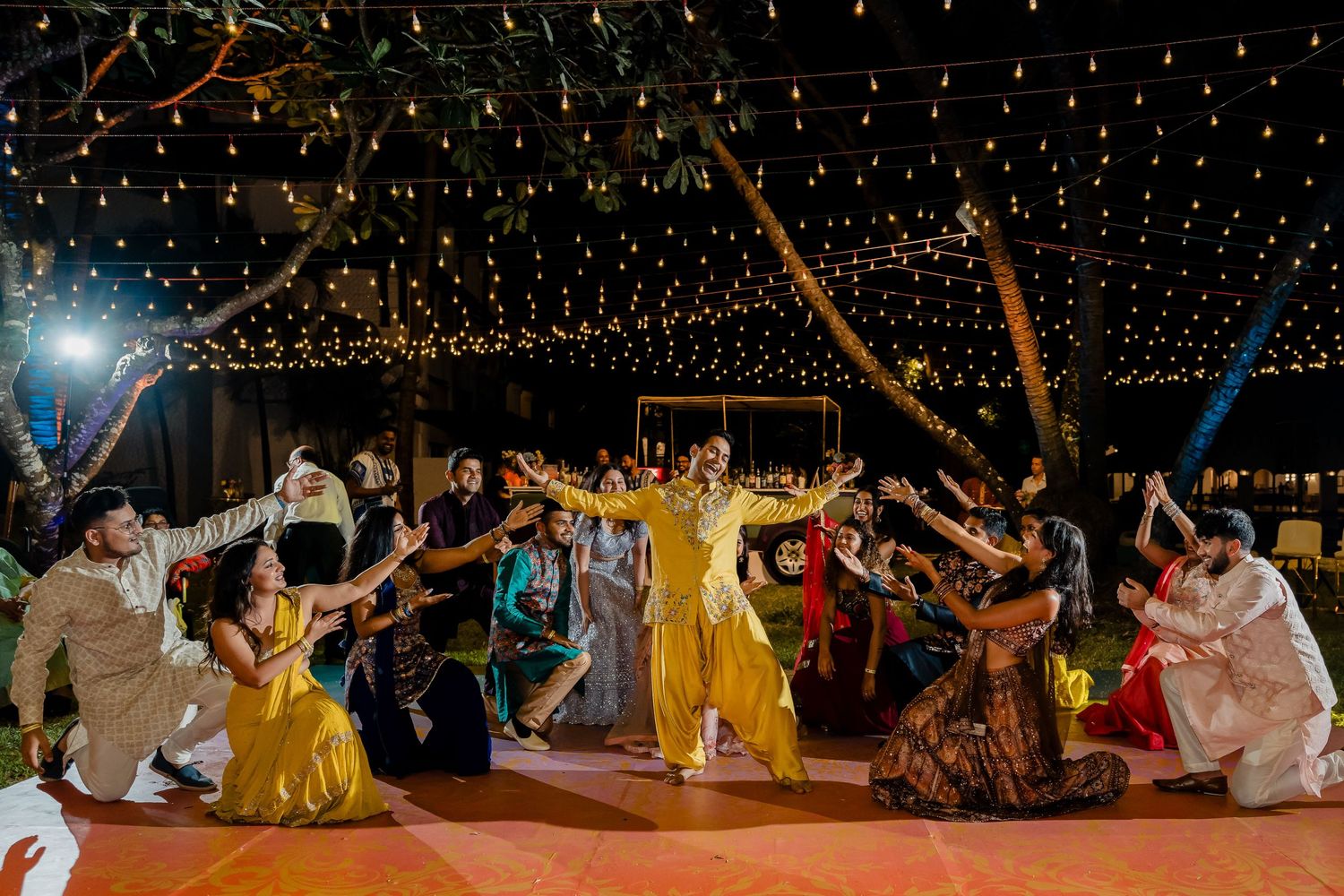 Celebratory dance circle under string lights with guests in colorful traditional attire.