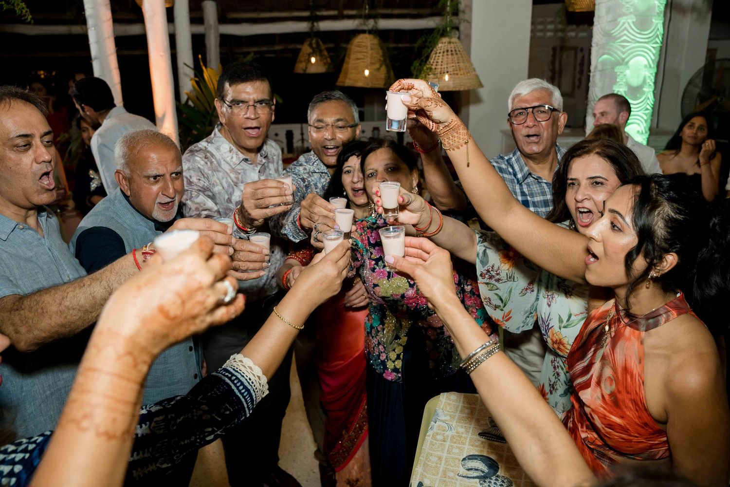 A crowd of wedding guests raise their glasses in a celebratory toast during a reception.