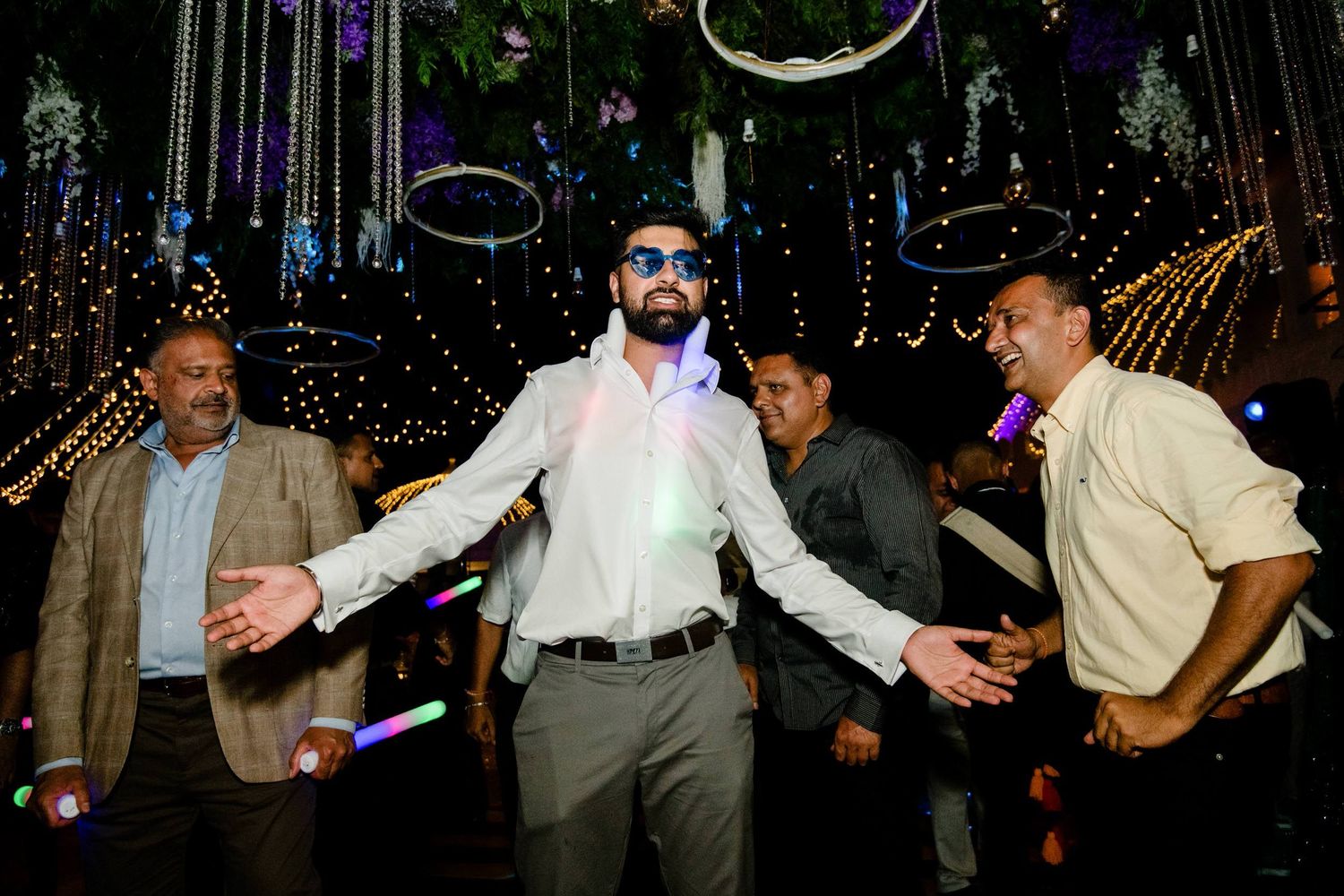 Party guests dancing and celebrating under decorative hanging lights in an evening celebration.