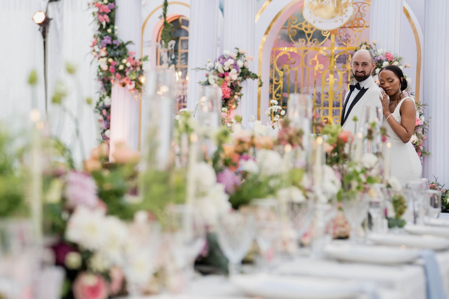 Elegant wedding reception table settings with pink and white floral centerpieces in a light-filled venue.
