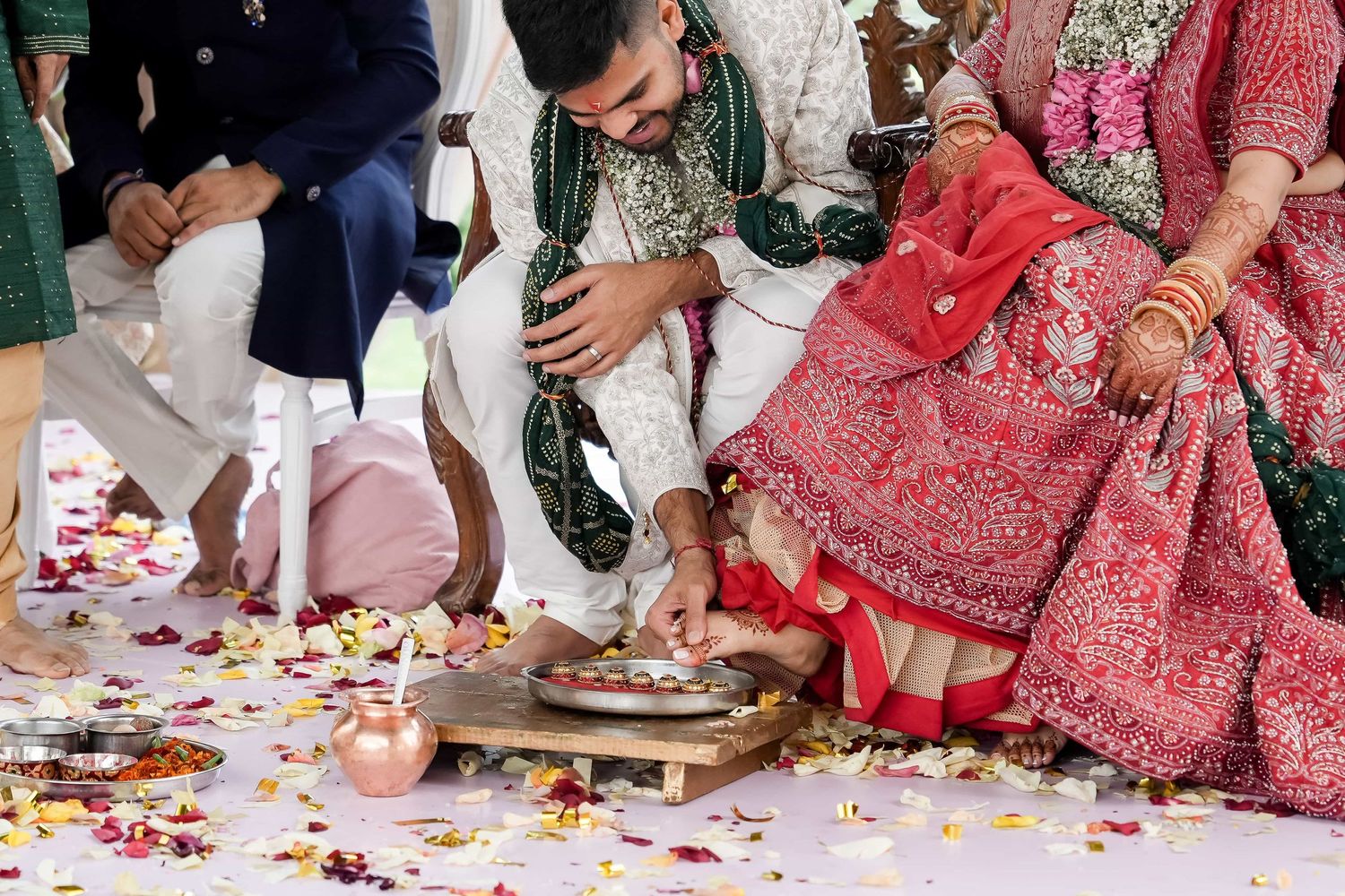 Traditional Indian wedding ceremony detail with rose petals scattered on floor and ornate red lehenga dress visible.