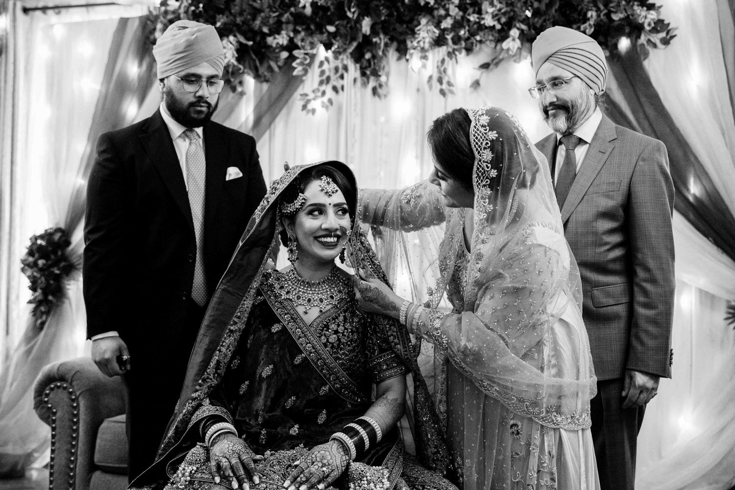 Black and white photo of a traditional Indian wedding ceremony with family members and decorative details.