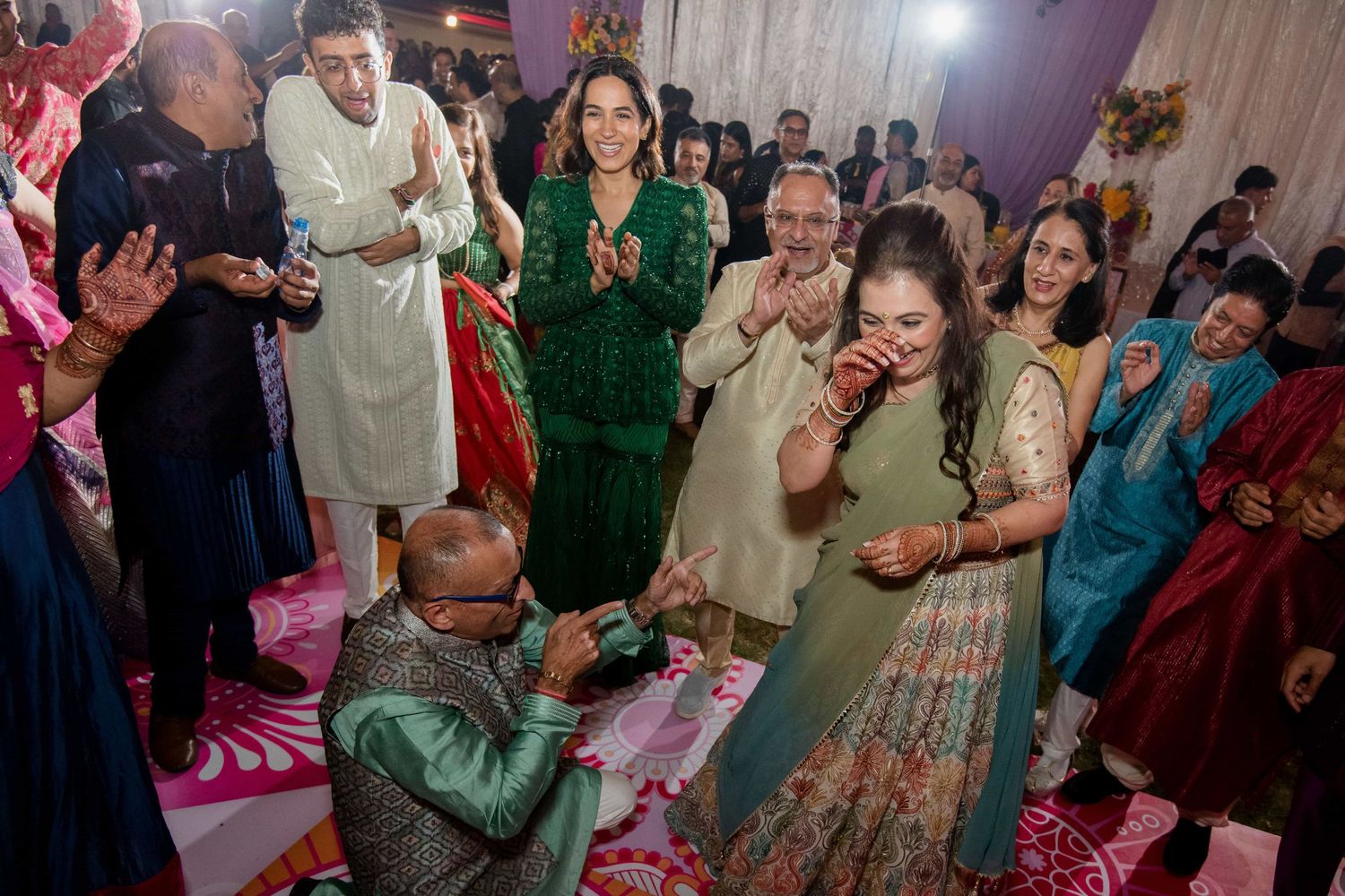Wedding guests celebrate with traditional dance moves on a pink-lit dance floor.