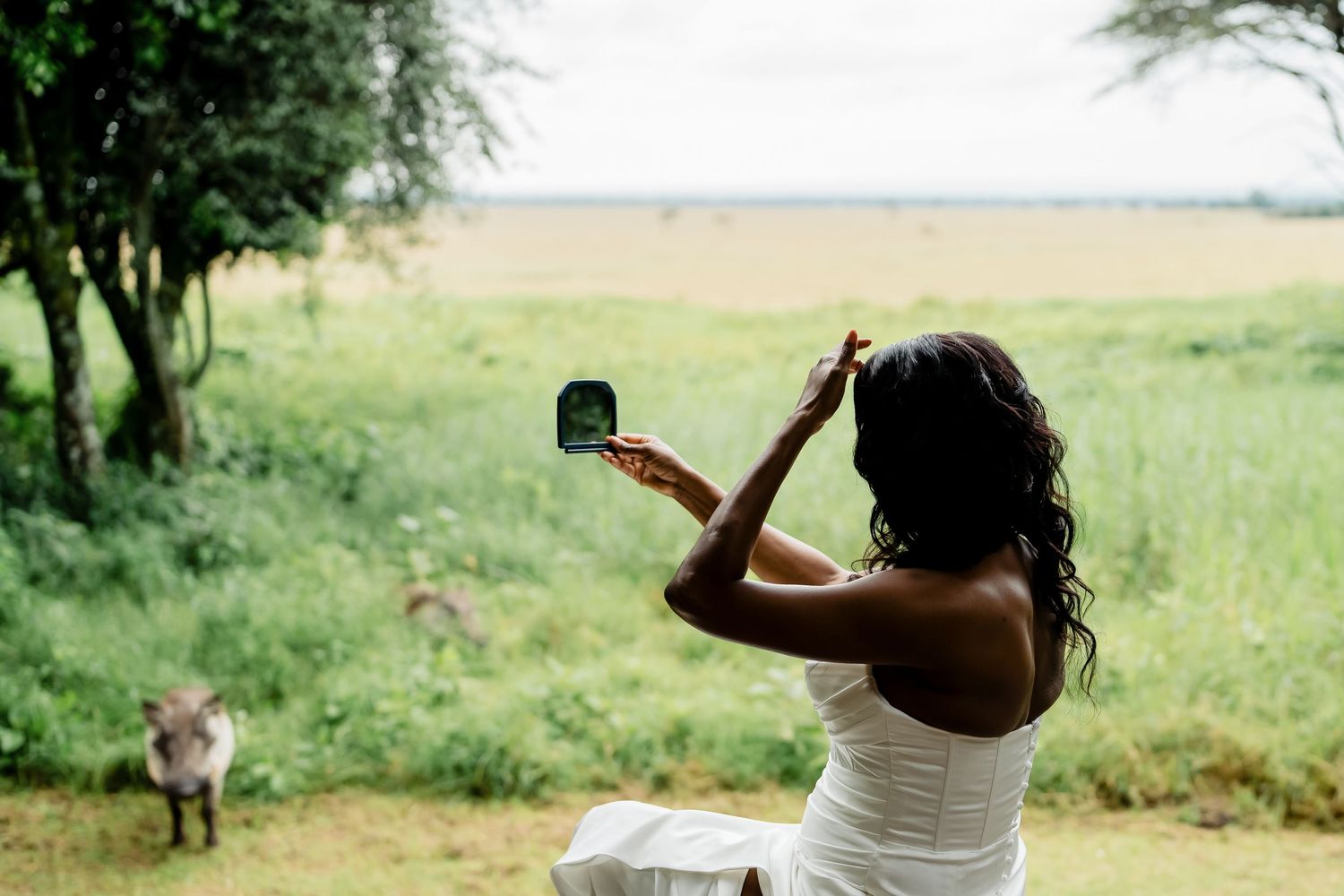 Someone in a white dress takes a photo of the scenic African savanna landscape with a camera.