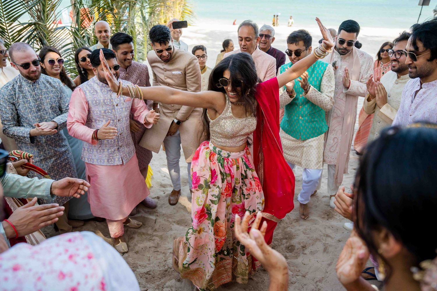 A lively group of people dancing and celebrating at an outdoor beach party with colorful attire.