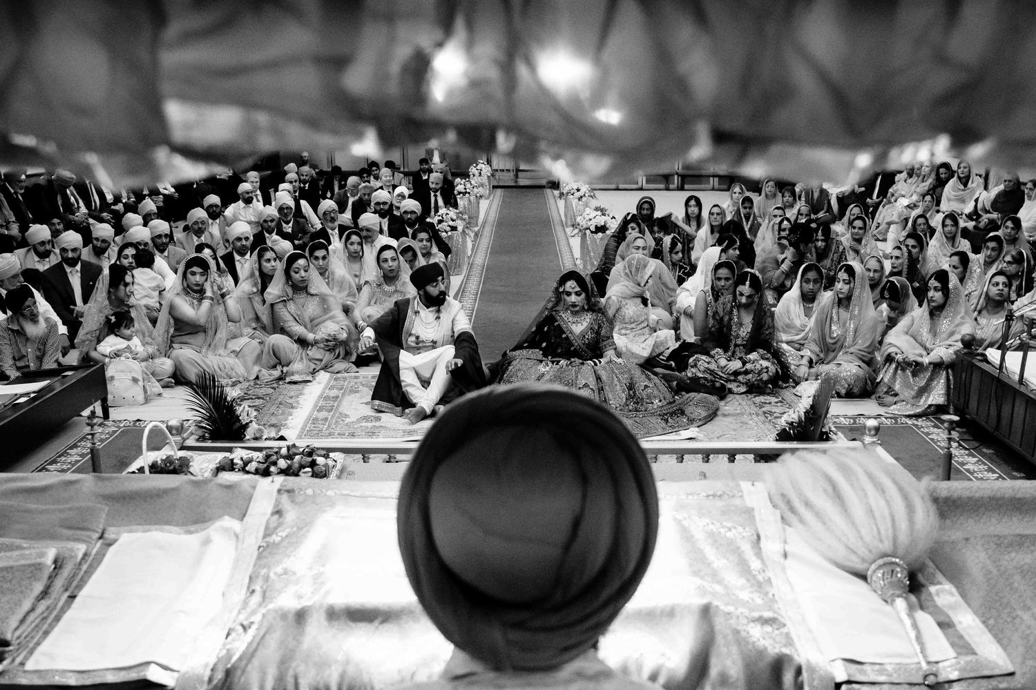 Black and white photograph of Sikh wedding ceremony showing gathering from unique perspective.