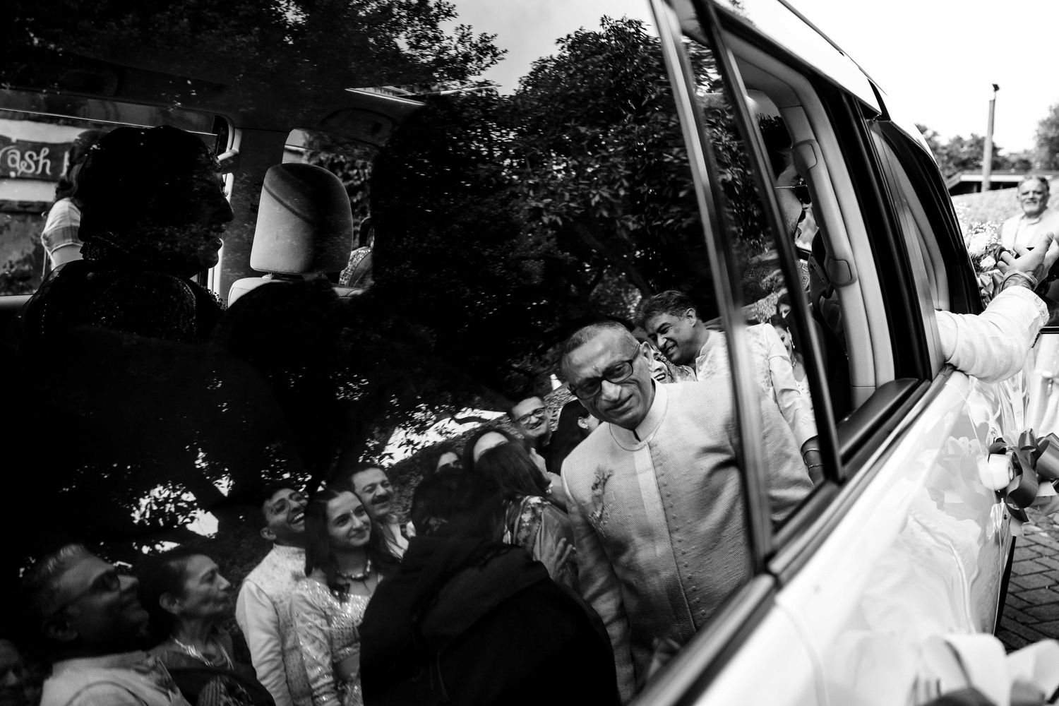 Black and white photo of wedding guests gathered around a limousine.