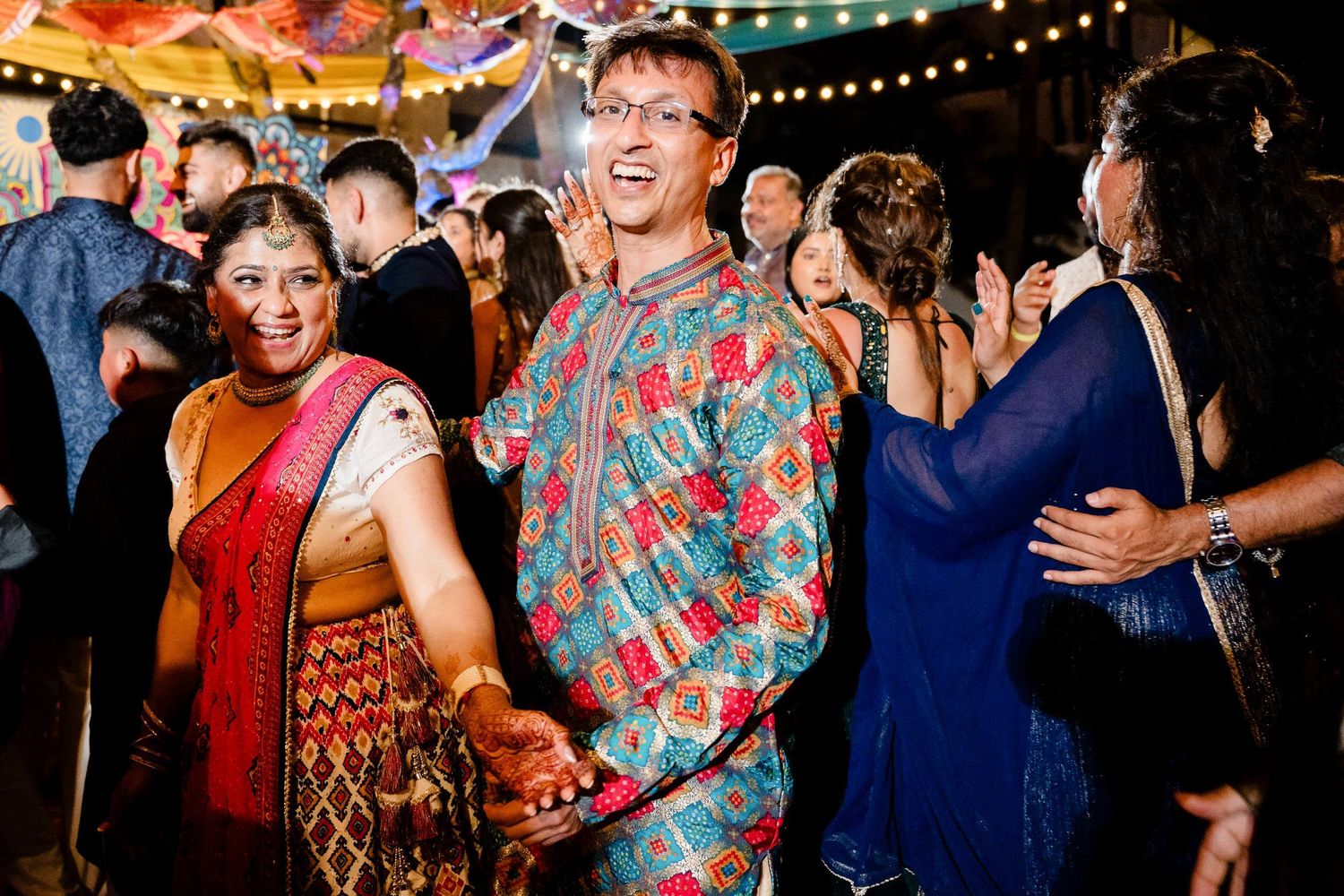 Joyful guests dancing and celebrating at a lively wedding reception with colorful lights and decor.