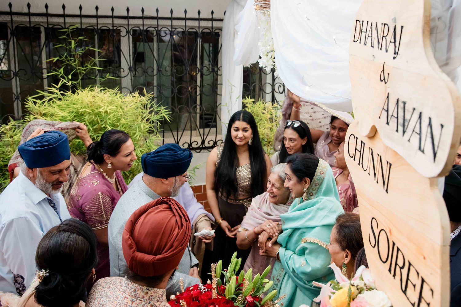 A festive Sikh wedding gathering with family members celebrating around decorative signs.