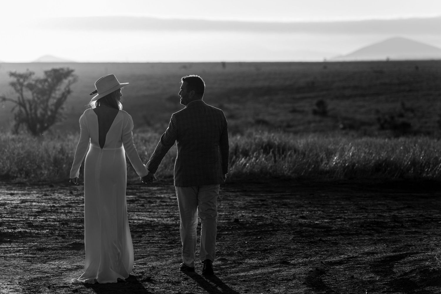 Black and white photo of a couple walking hand in hand across a desert landscape.