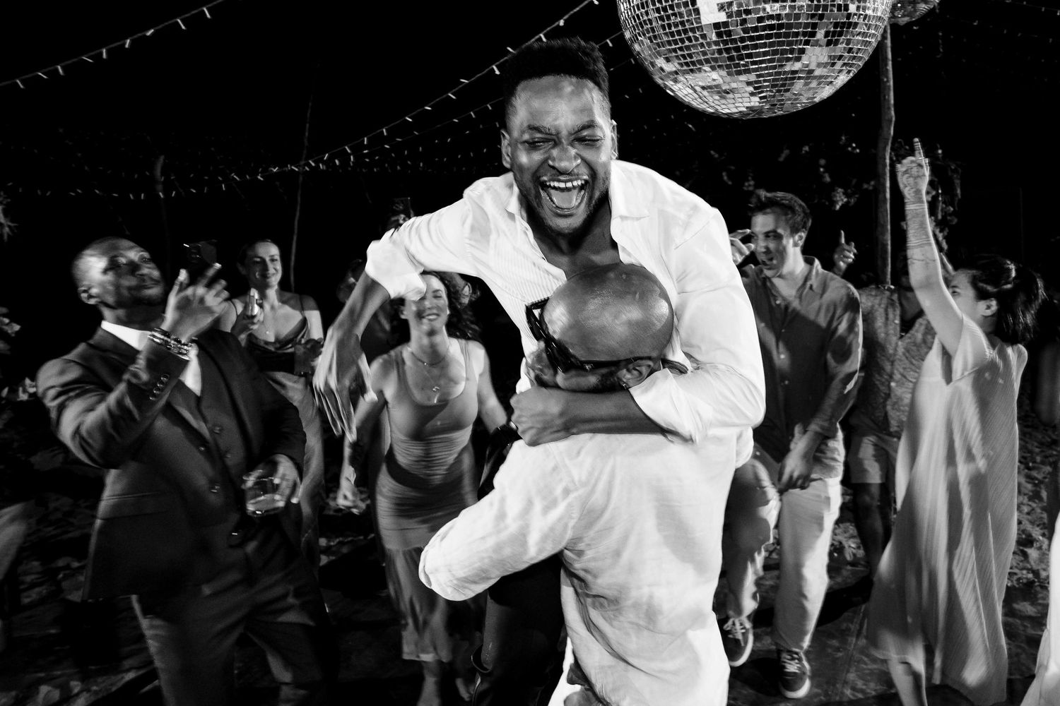 People dance and celebrate under a disco ball at what appears to be a lively party or reception.