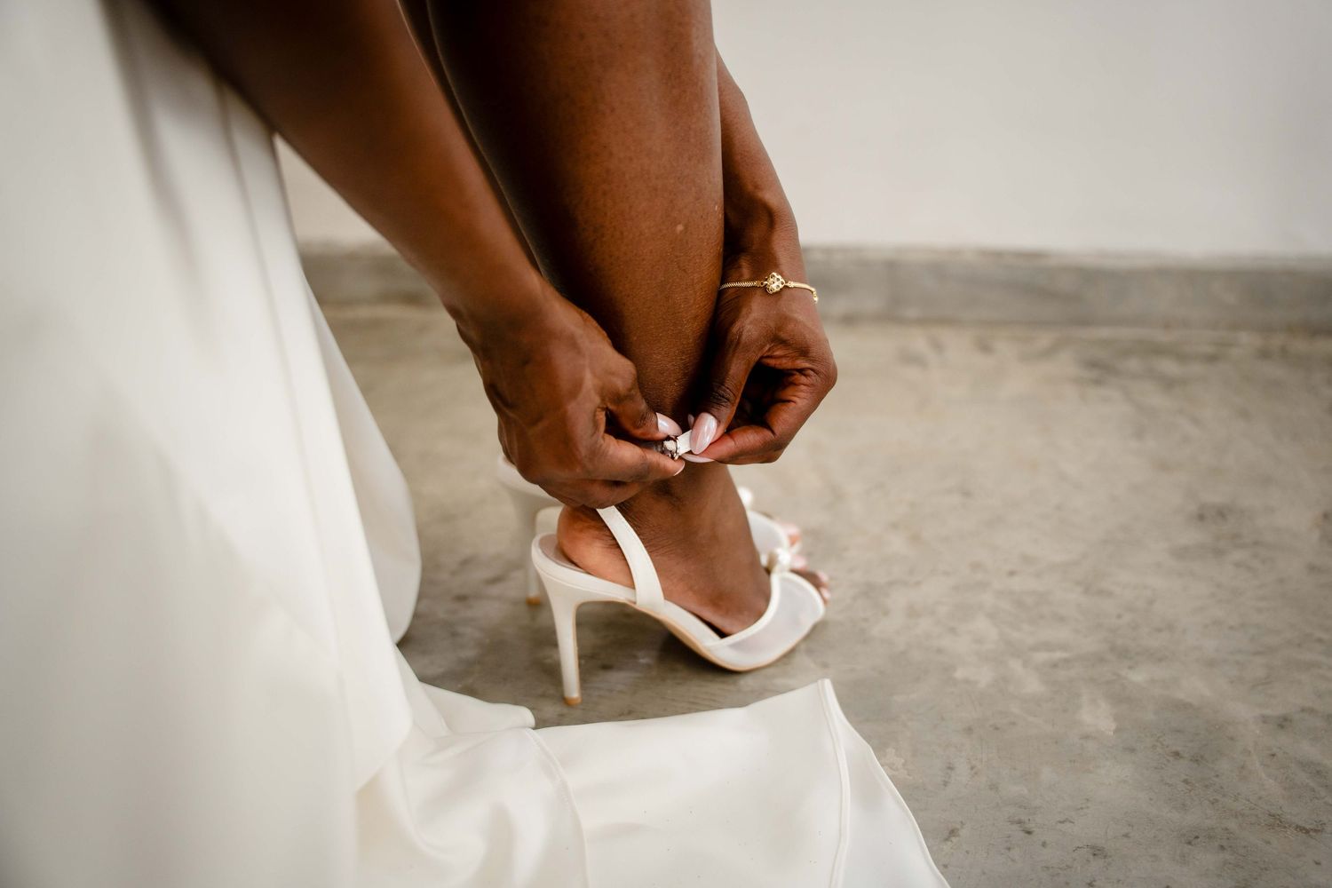 Close-up view of hands putting on elegant white bridal heels before a wedding ceremony.