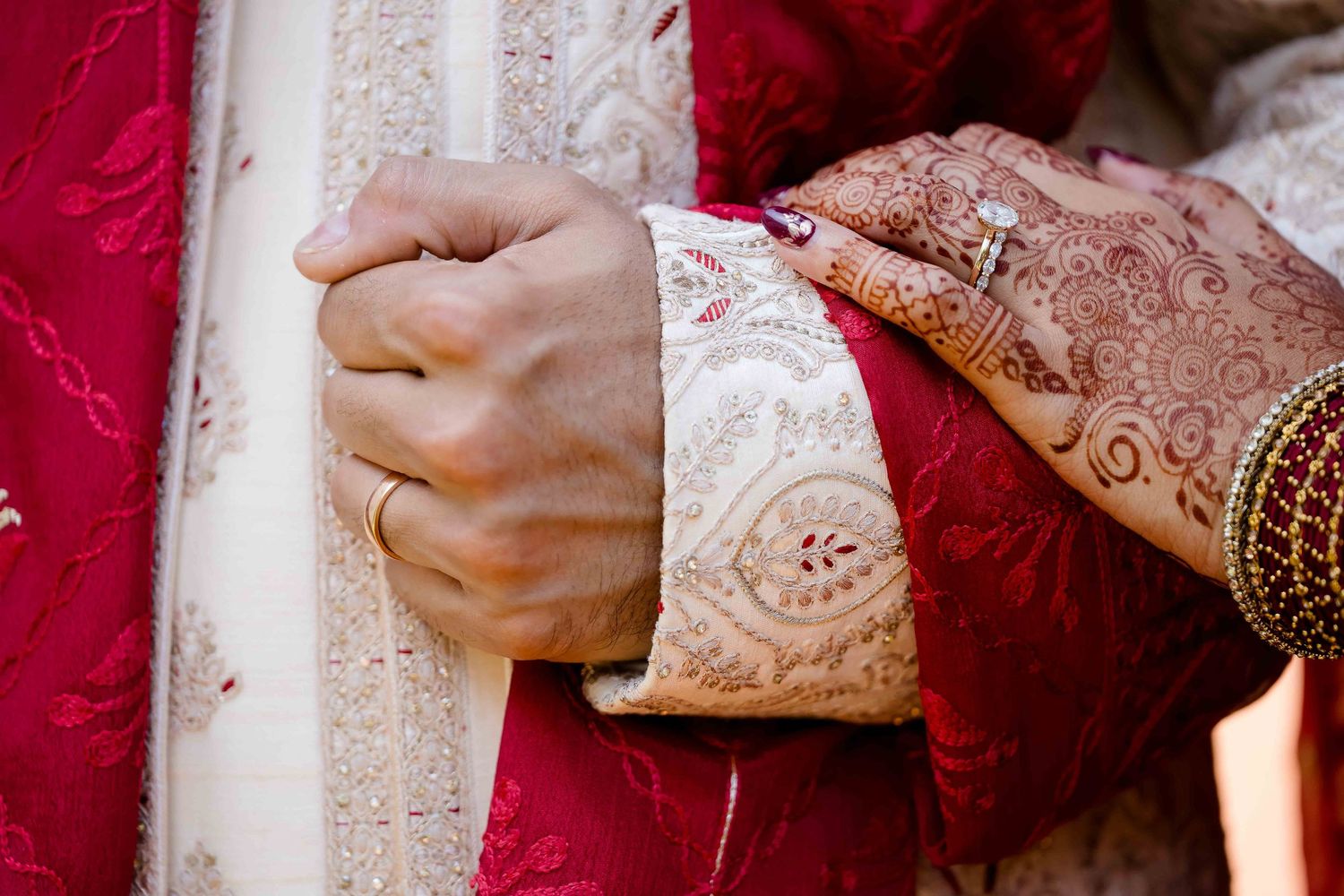 Hands adorned in traditional Indian wedding attire hold decorative elements against an ornate pink and white backdrop.