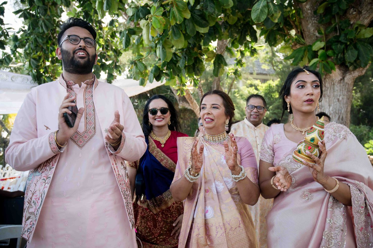 A group celebrates outdoors under green trees during a festive summer gathering.