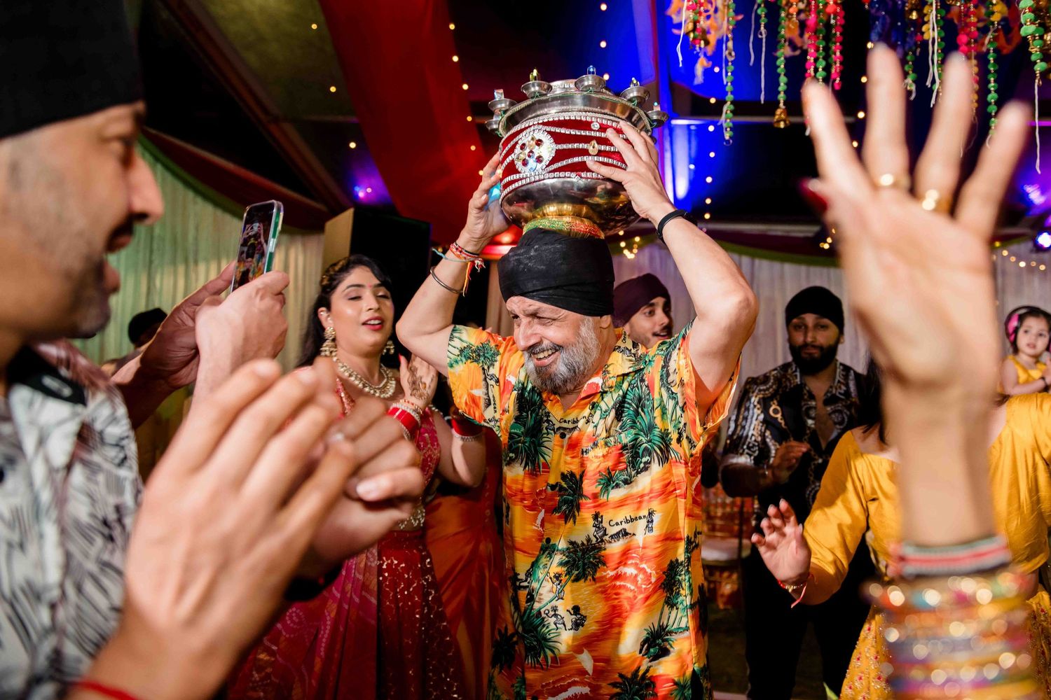 Celebratory moment at Indian wedding with colorful lights and decorations in background.