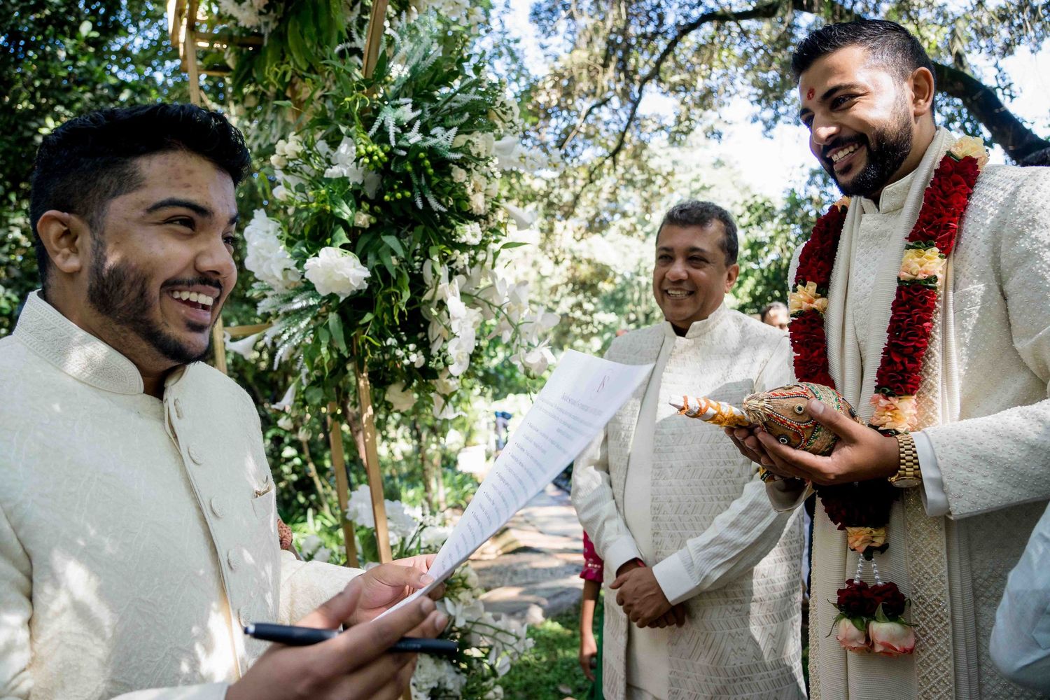 Traditional South Asian wedding ceremony with men in white traditional attire exchanging items outdoors.