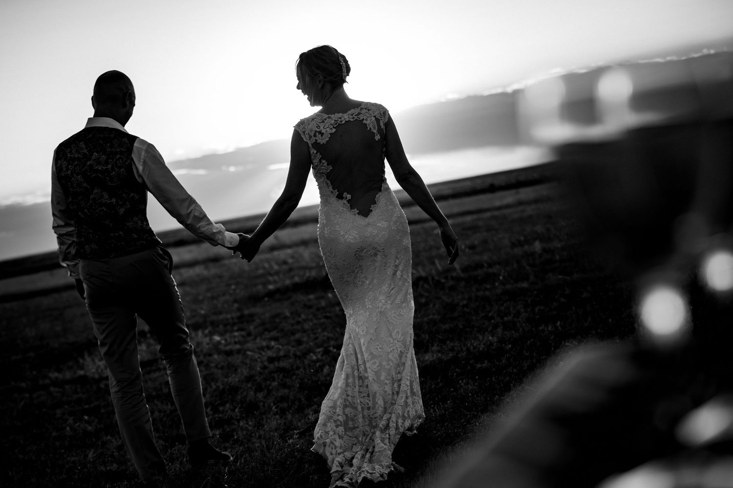 Silhouettes of couples walking along a misty beach at sunset in black and white.