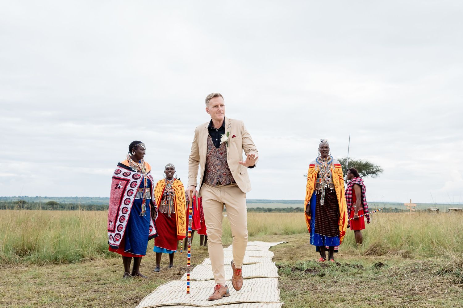 Traditional Maasai people in colorful clothing walk along a path in the African savanna.