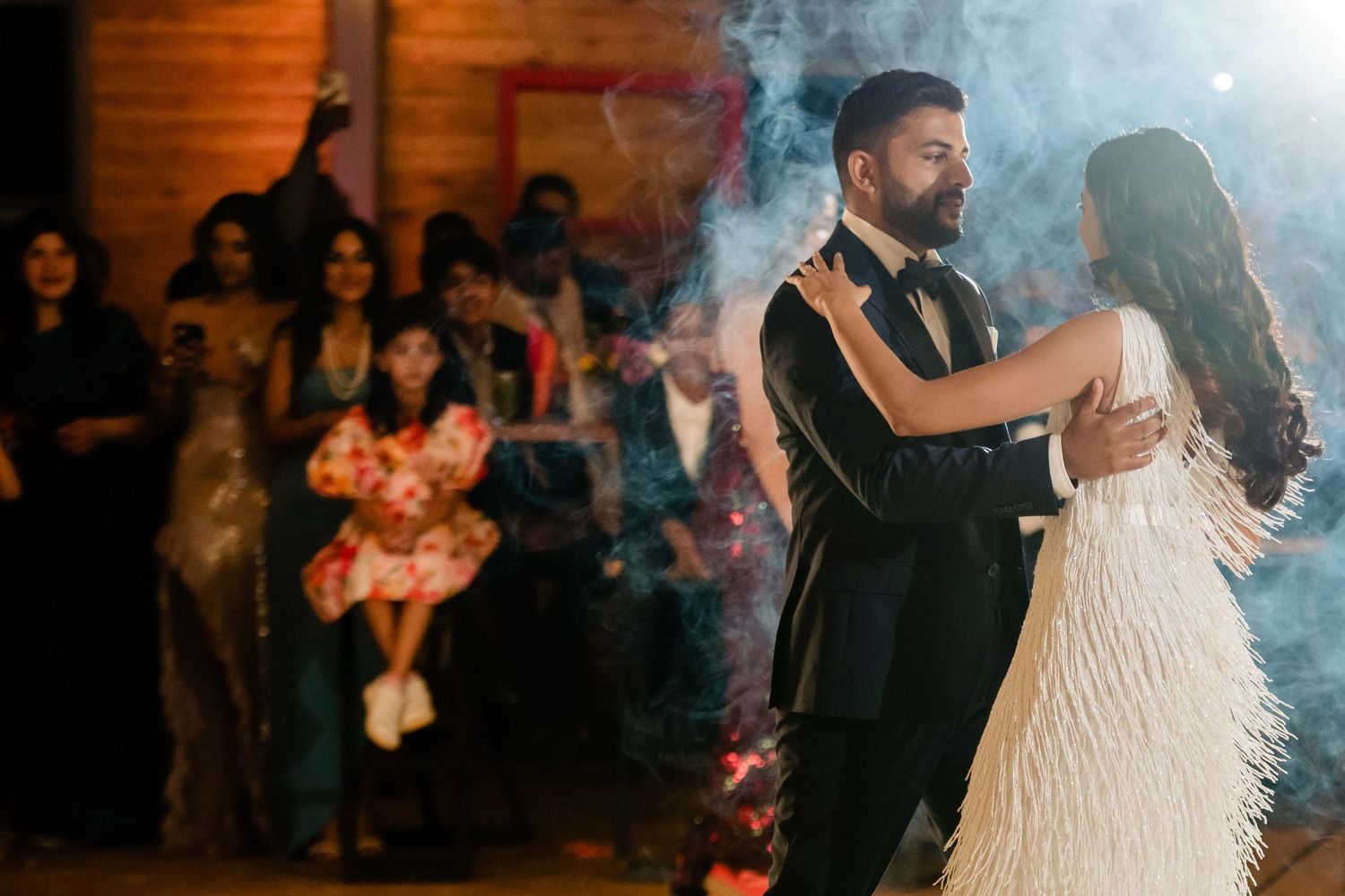 A couple shares their first dance at a wedding reception with smoke effects and mood lighting.