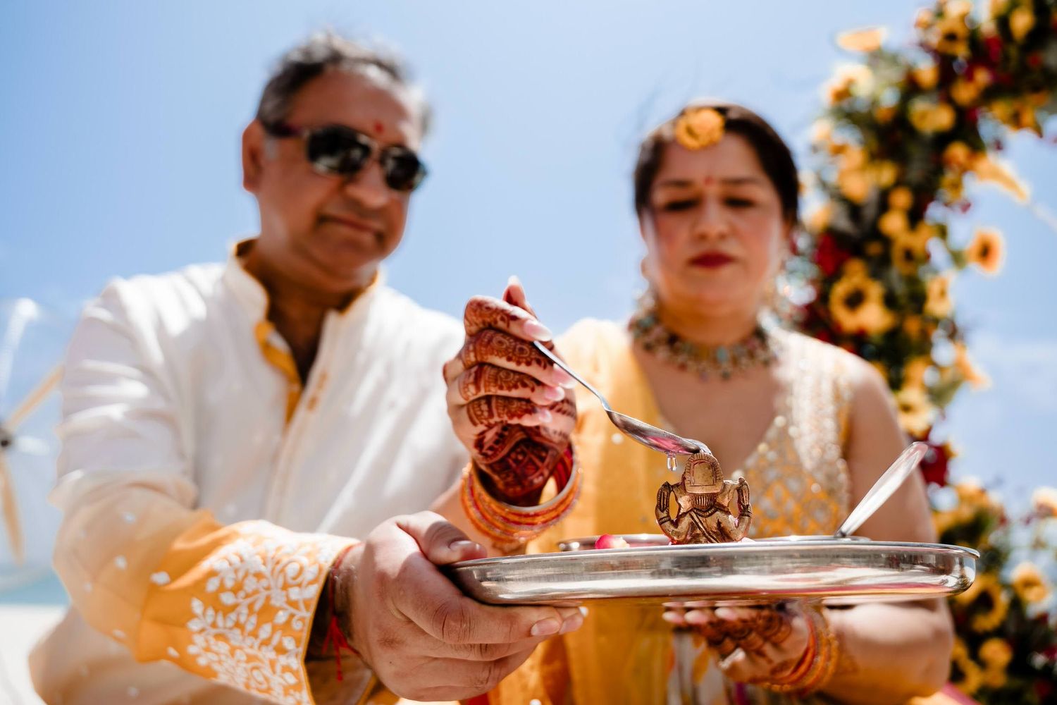 Wedding guests participate in traditional Indian ceremony rituals under bright sunlight.