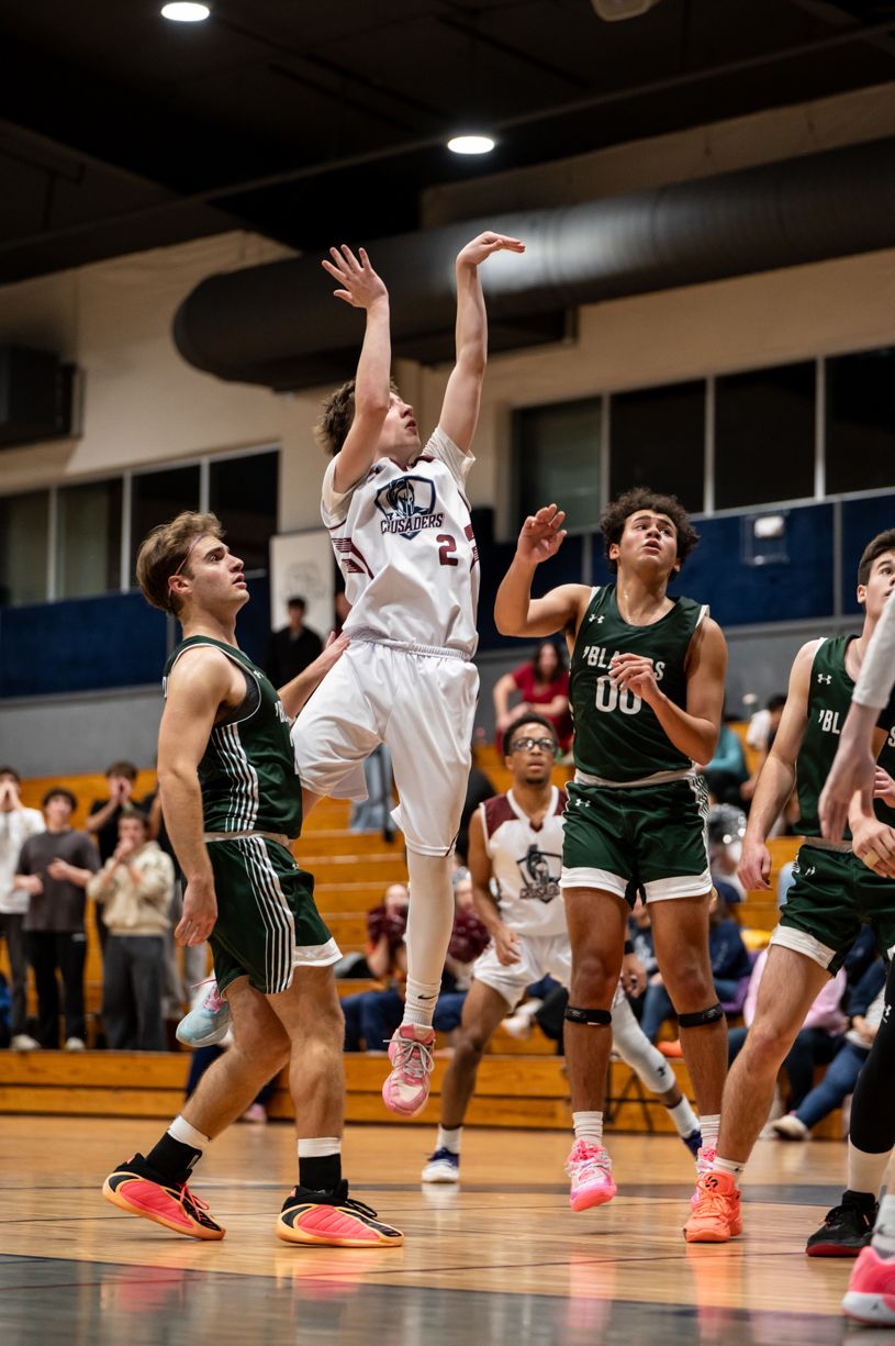 Basketball players jump for the ball during intense game action on indoor court.