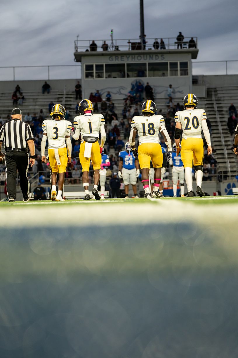 Football team in yellow uniforms lined up on sideline during evening game.