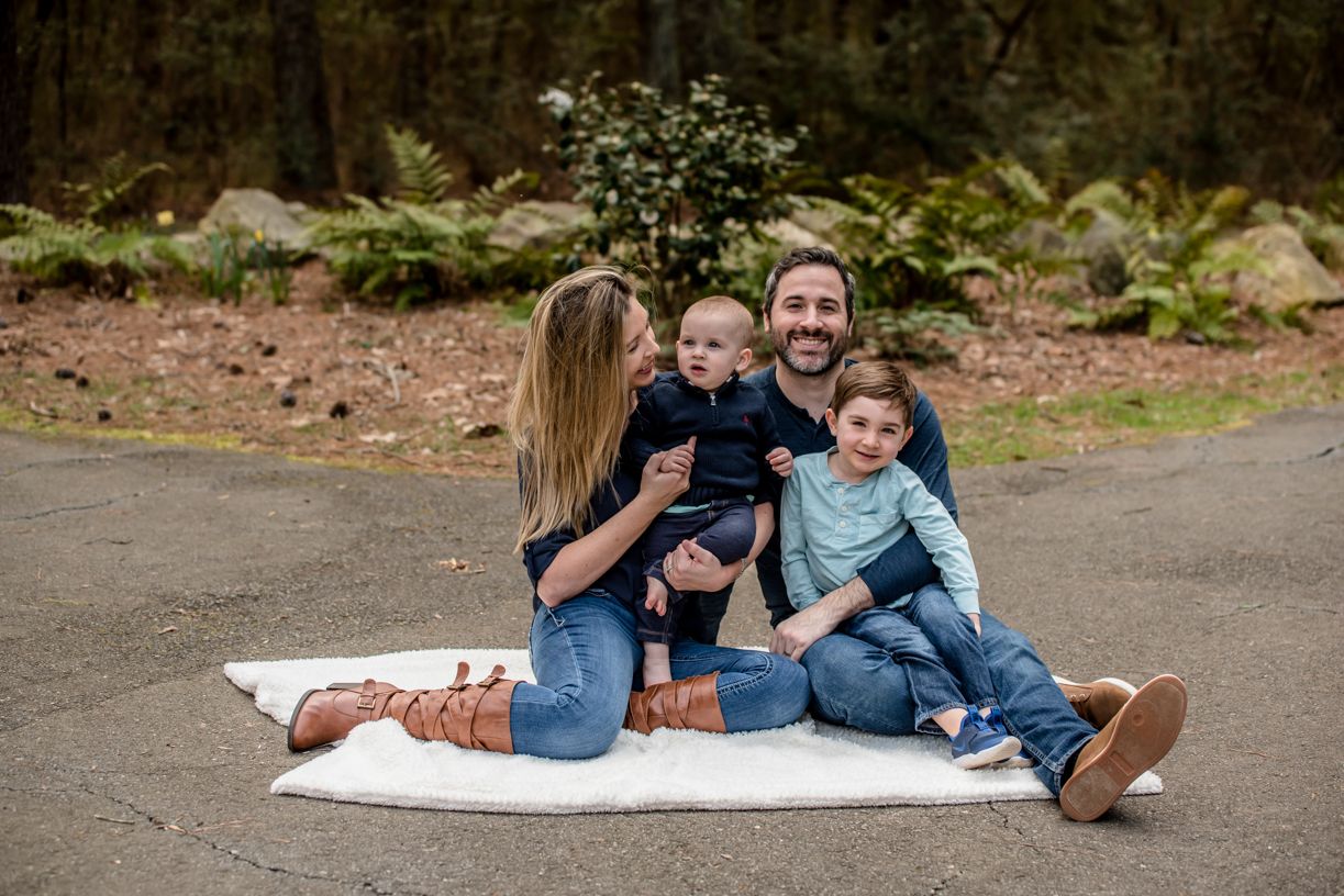 Family of four sitting on blanket outdoors for casual portrait session.