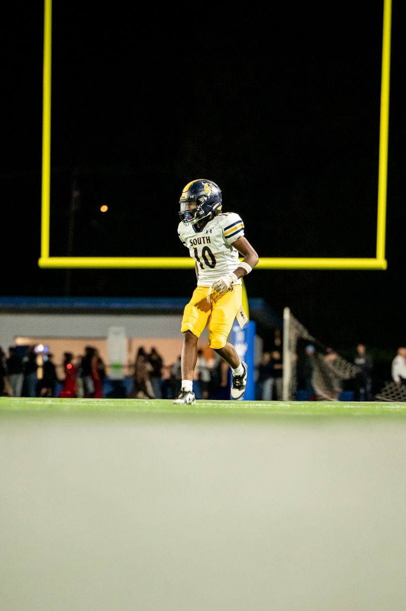 Football player in yellow uniform running on field at night.