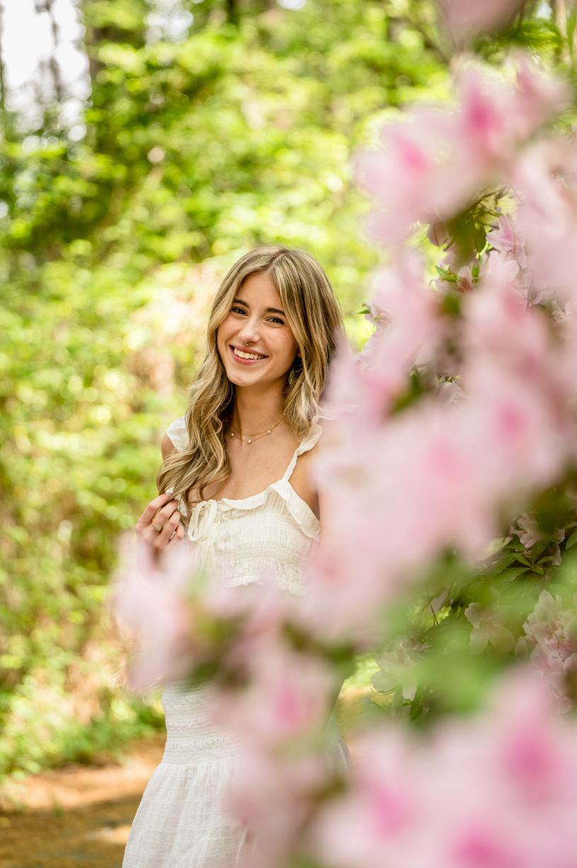 Spring portrait session of a senior girl with white lace dress among blooming cherry blossoms.