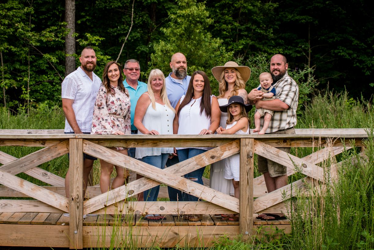 Large group portrait of people standing together on wooden bridge in summer forest setting.