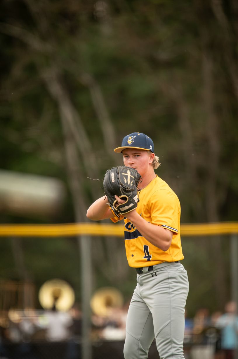 Baseball player in yellow jersey and gray pants winds up to pitch on a sunny day.