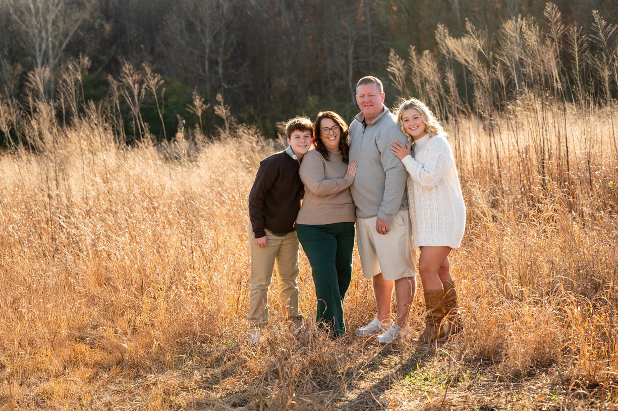 Family group photo in a golden field with tall grass during sunset.