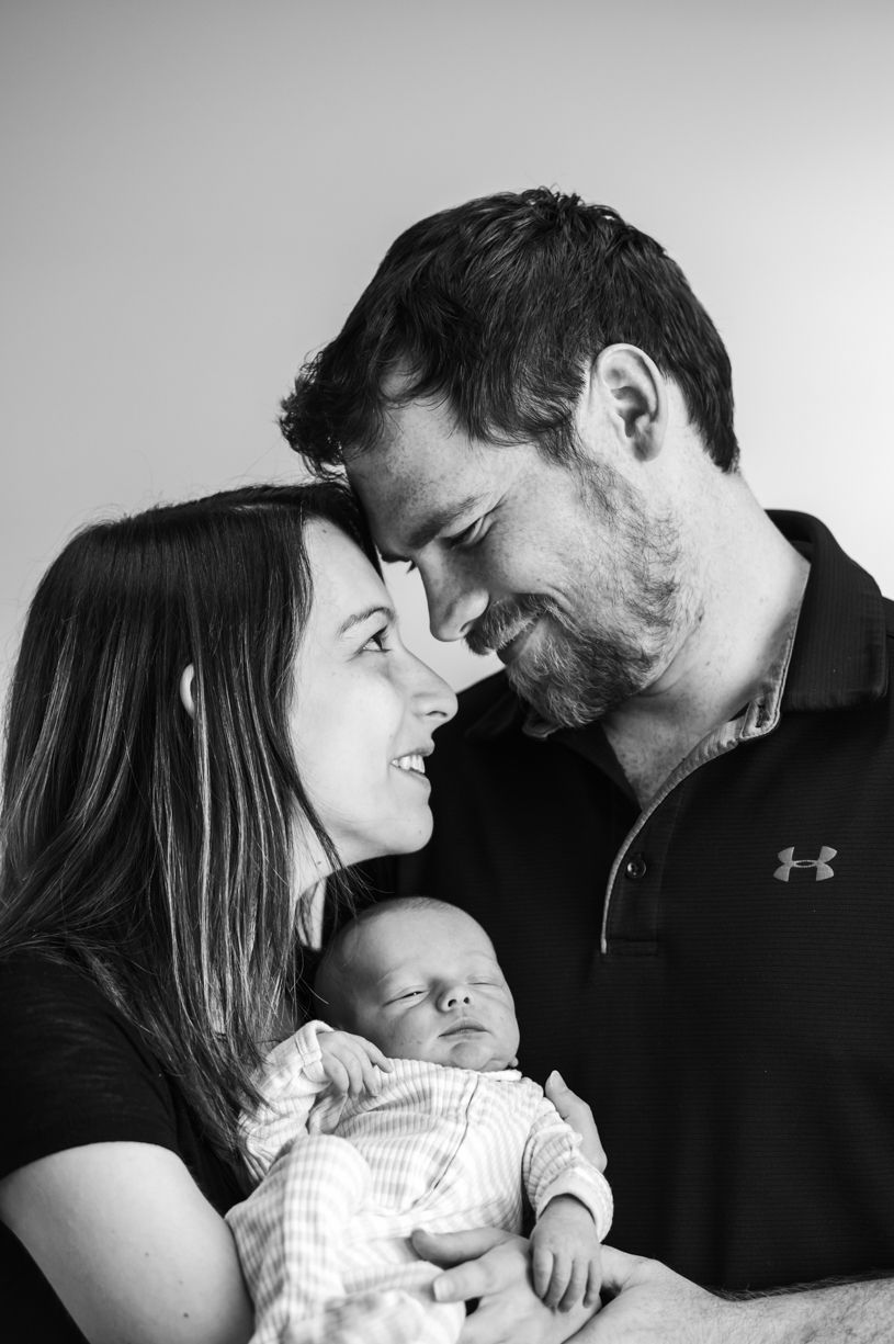 Black and white portrait of new parents sharing intimate moment with sleeping baby.