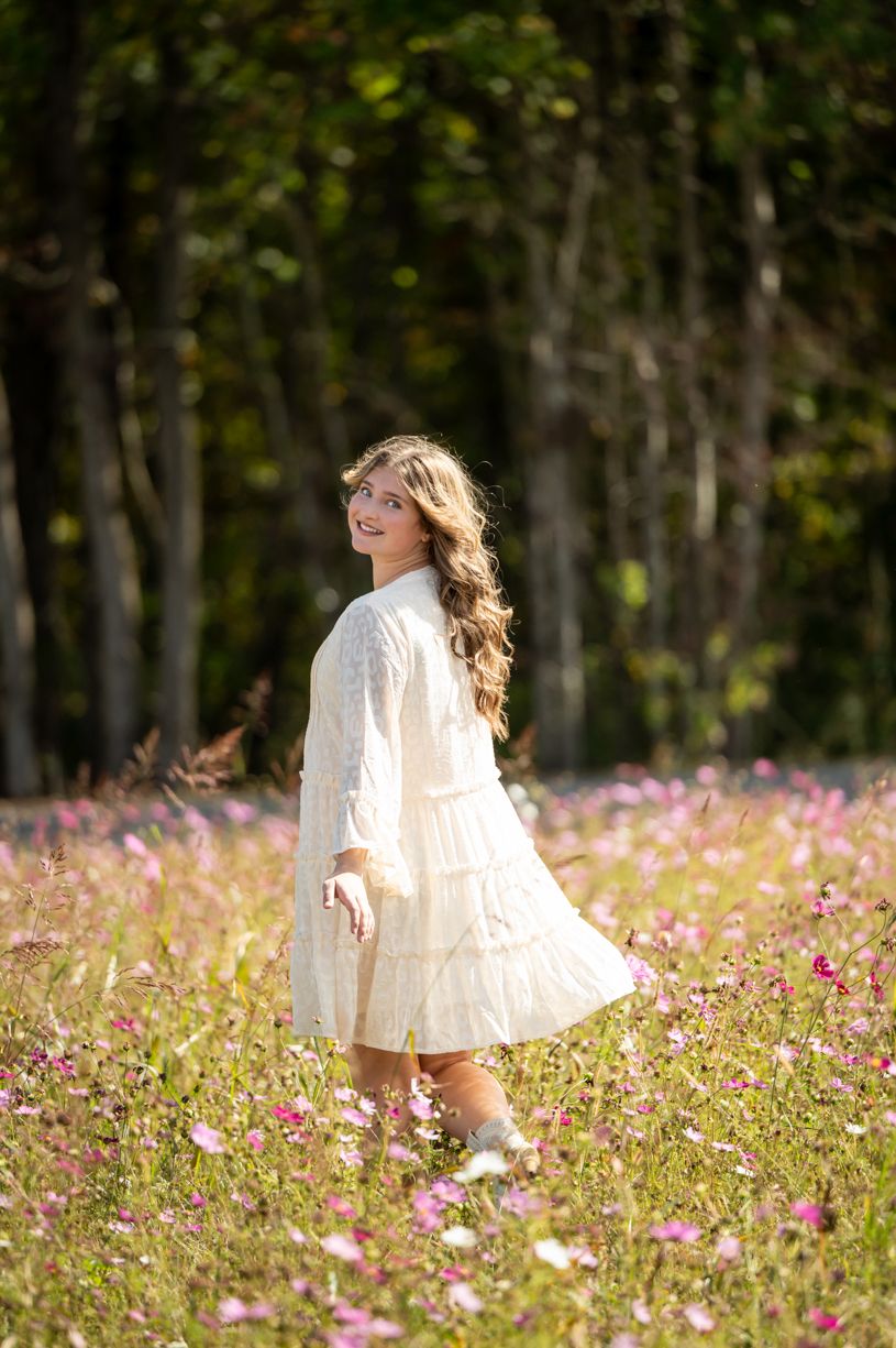 A senior girl wearing flowing white dress twirls through a field of wildflowers.