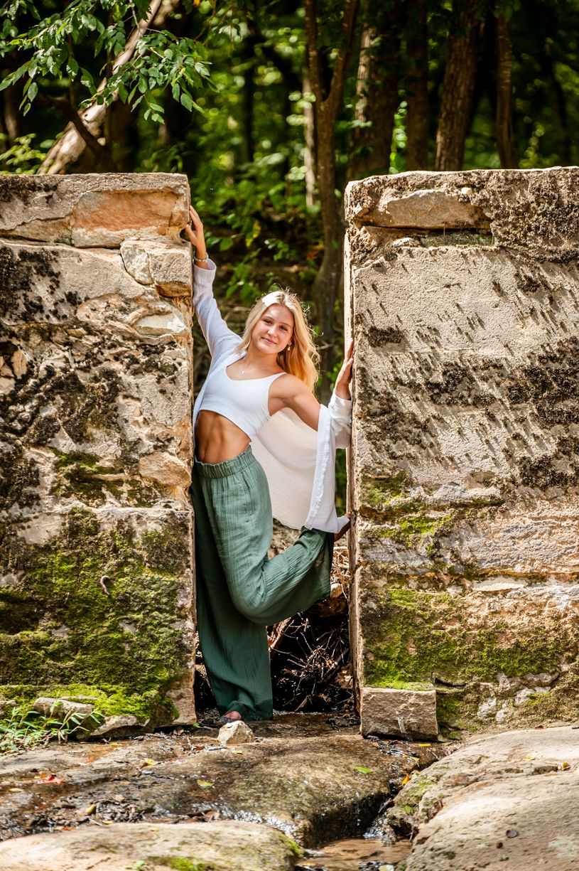Senior portrait session in a rustic stone setting with green overalls.