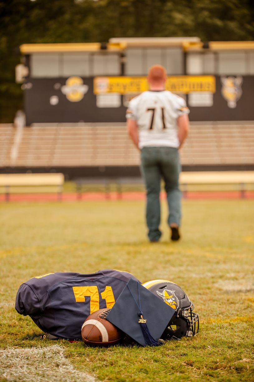 Football jersey and equipment laid out on field with senior player walking away in background.