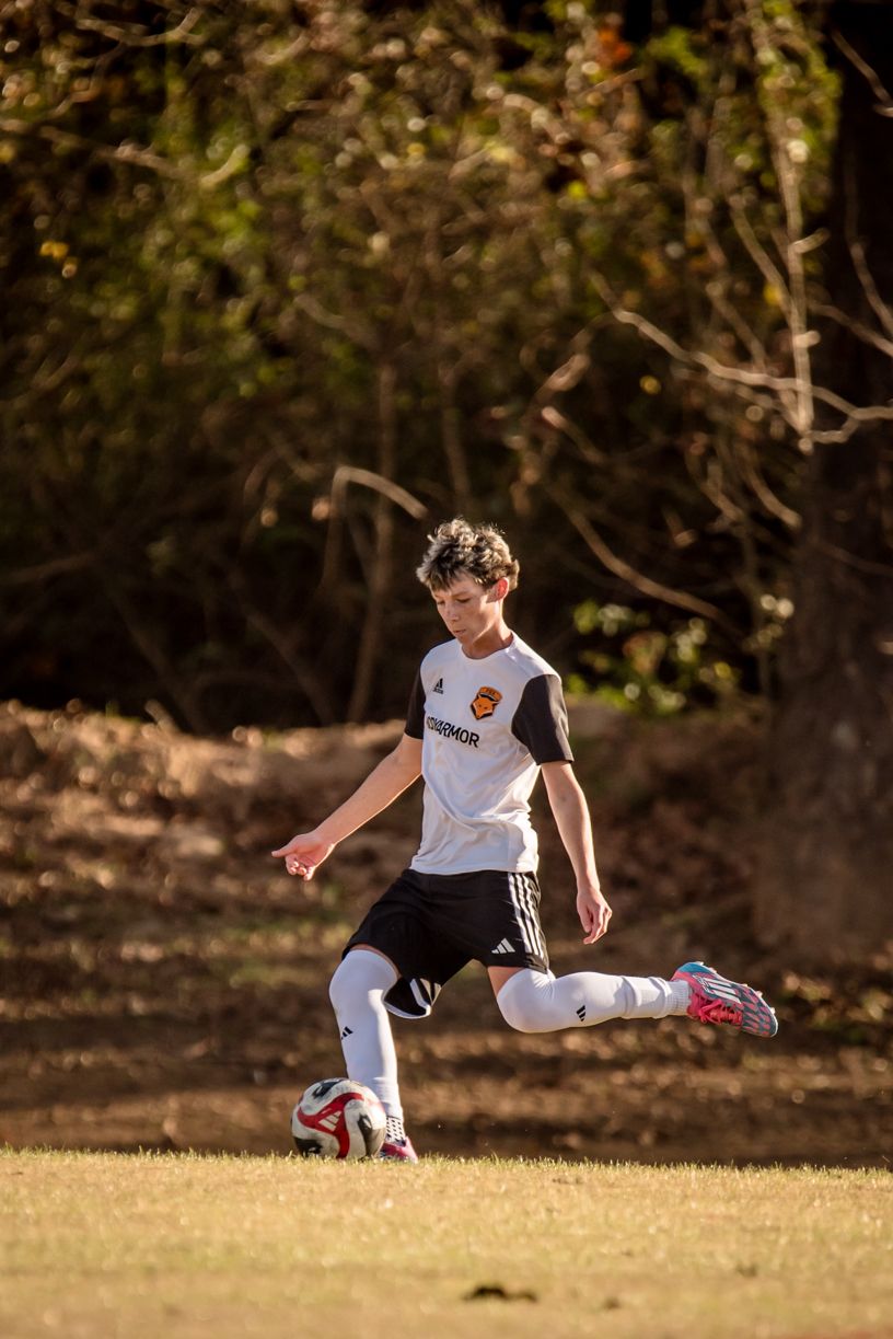 Soccer player in white jersey practicing kicks on a grassy field at sunset.