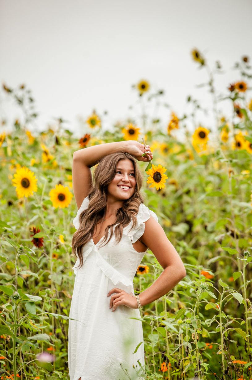 Joyful summer senior girl portrait in a vibrant sunflower field with white dress and natural lighting.
