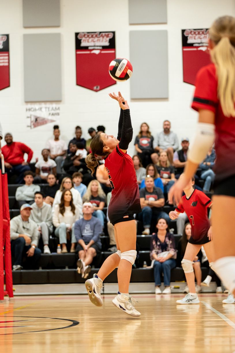 Volleyball players in red uniforms preparing to serve during an indoor match.