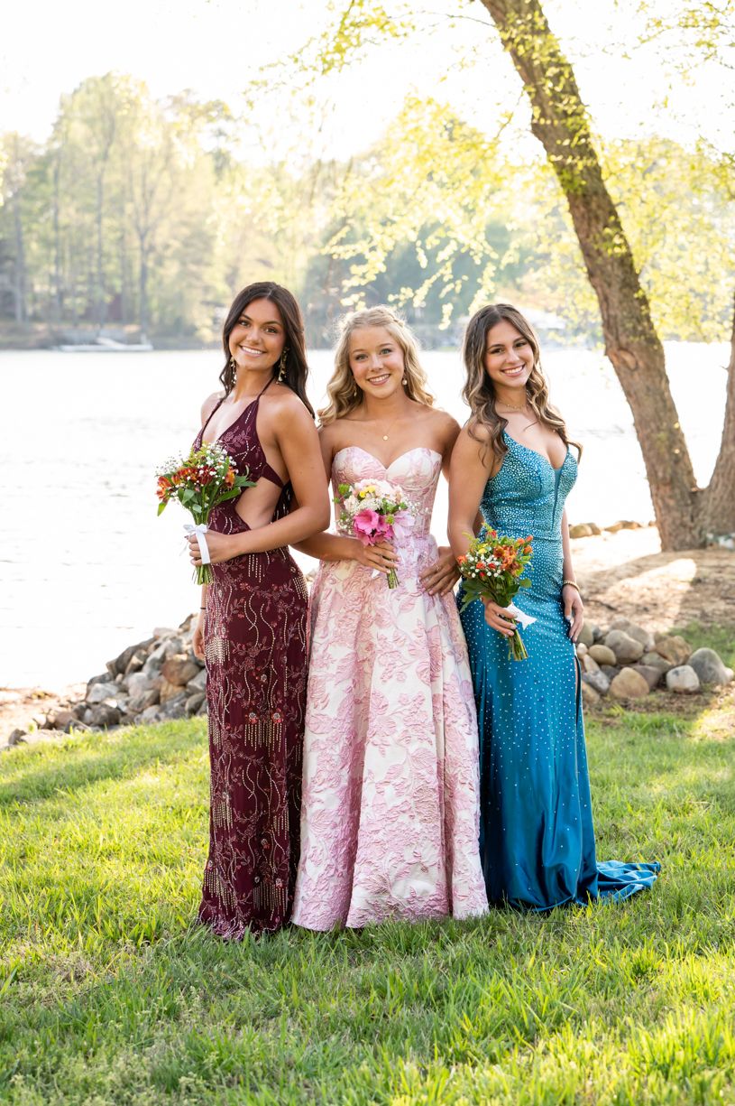 Friends in formal prom dresses posing together by a lake.