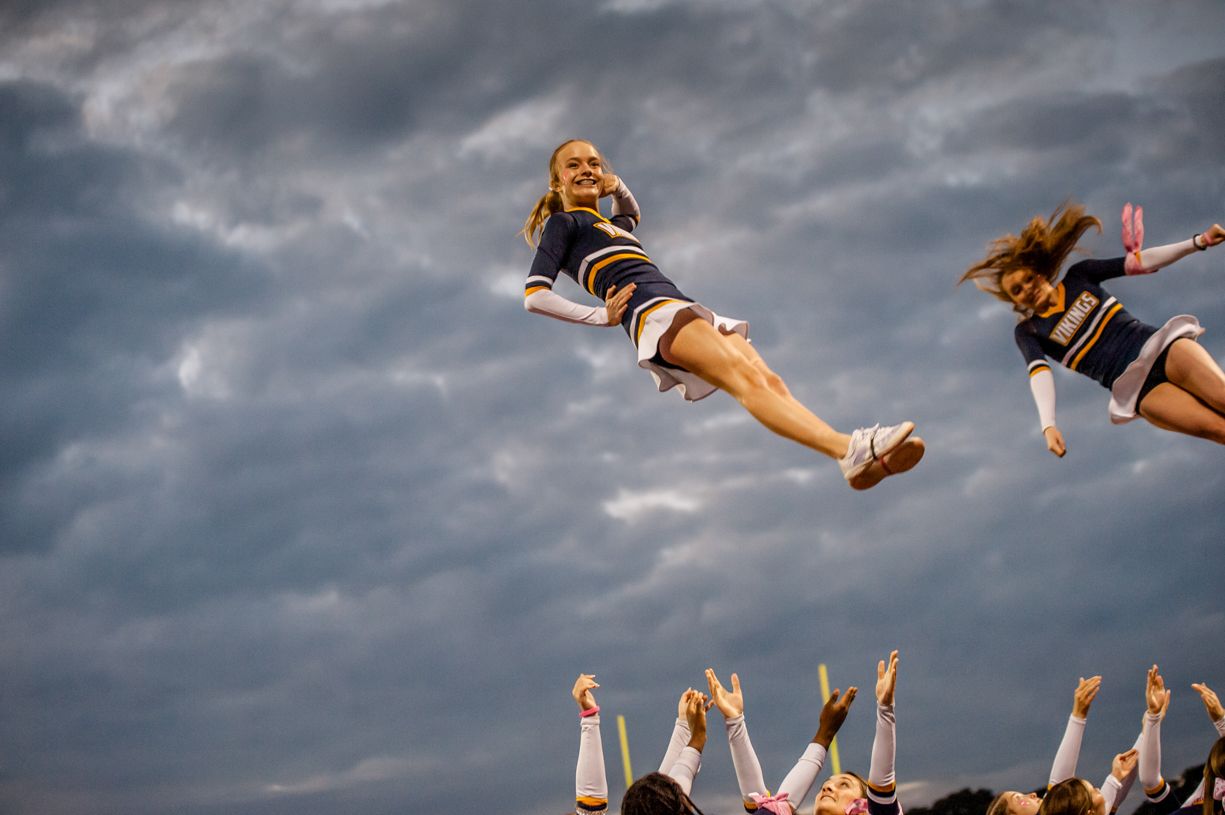 Group of cheerleaders being thrown into the air against dramatic cloudy sky.