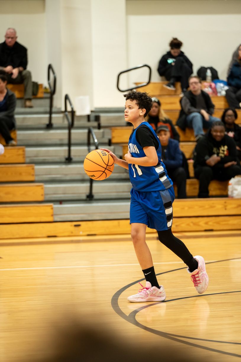 Basketball player in blue uniform dribbles ball during game in gymnasium.