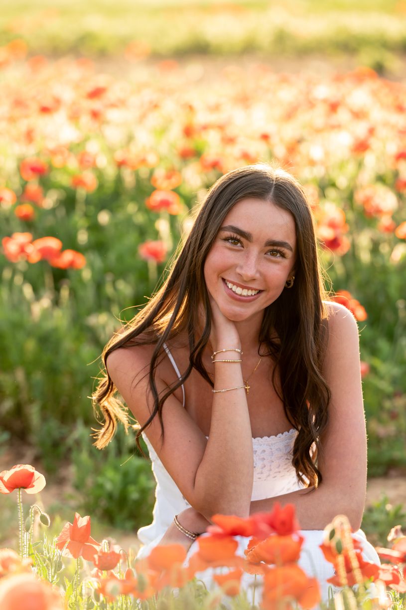 Dreamy outdoor portrait session of a senior girl in a field of vibrant orange poppies at golden hour.