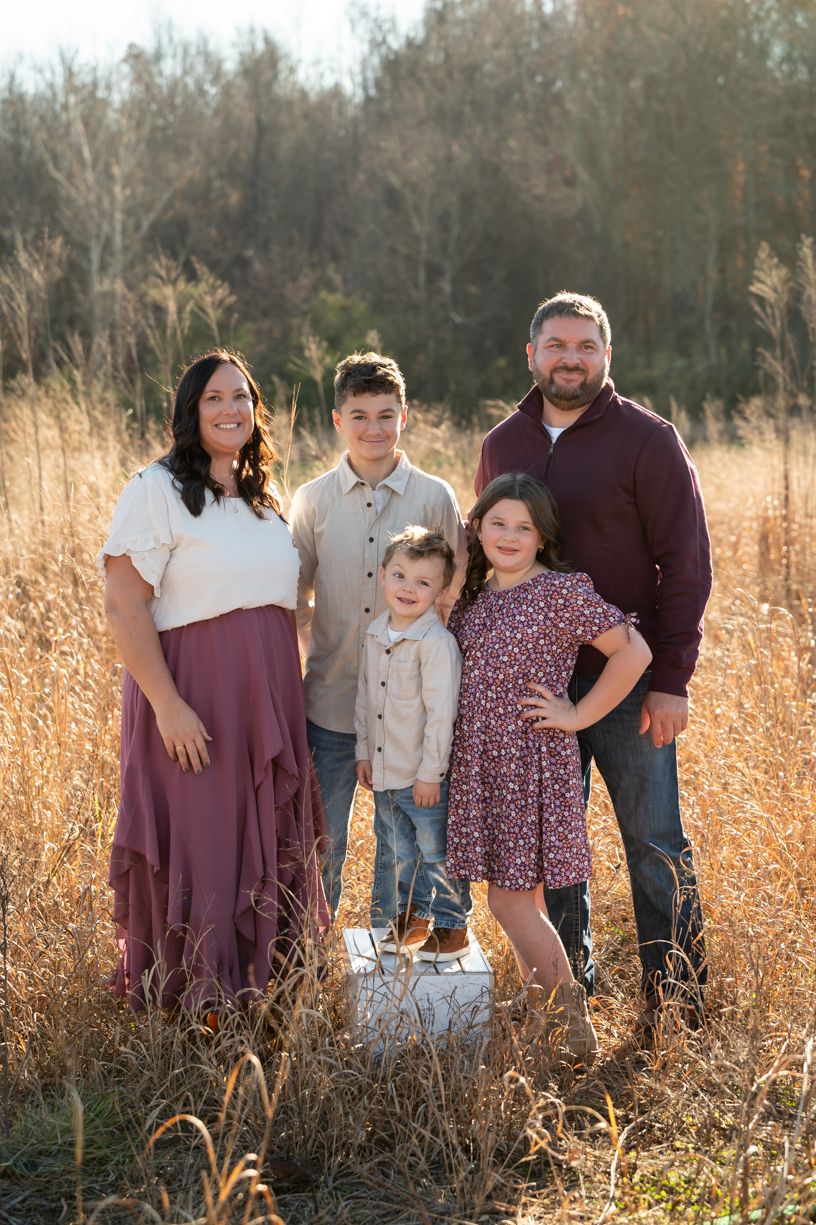 Family portrait session in a golden field during sunset wearing coordinated burgundy outfits.