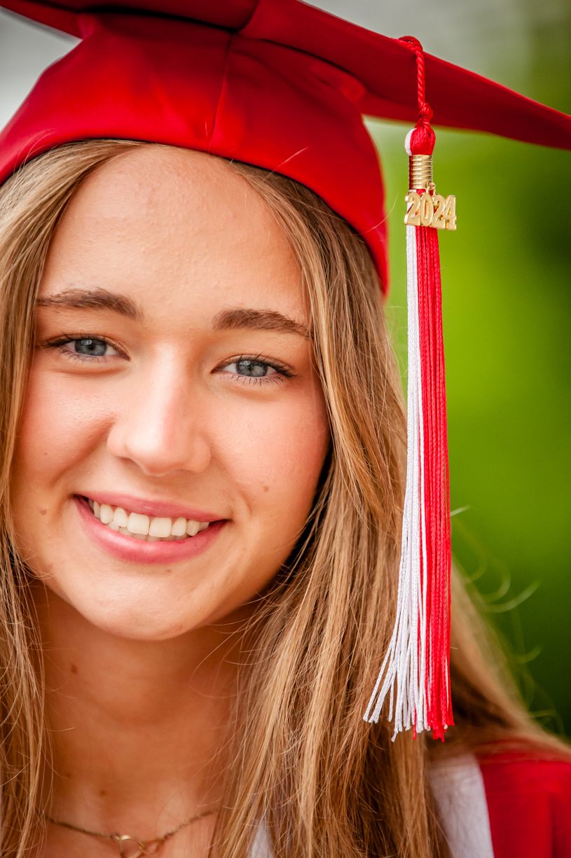 Graduate wearing red cap and gown with tassel smiles for portrait photo.