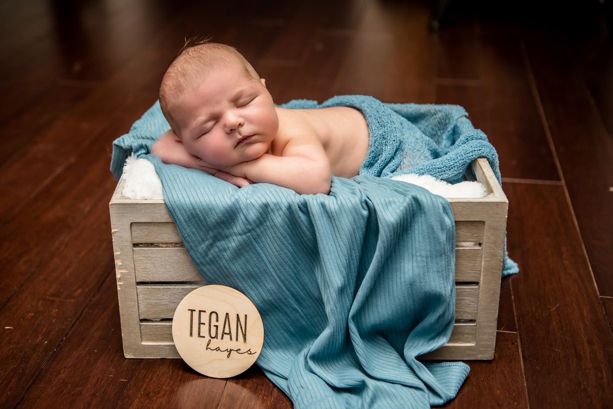 A sleeping newborn rests peacefully in a wooden crate with soft blue blankets.