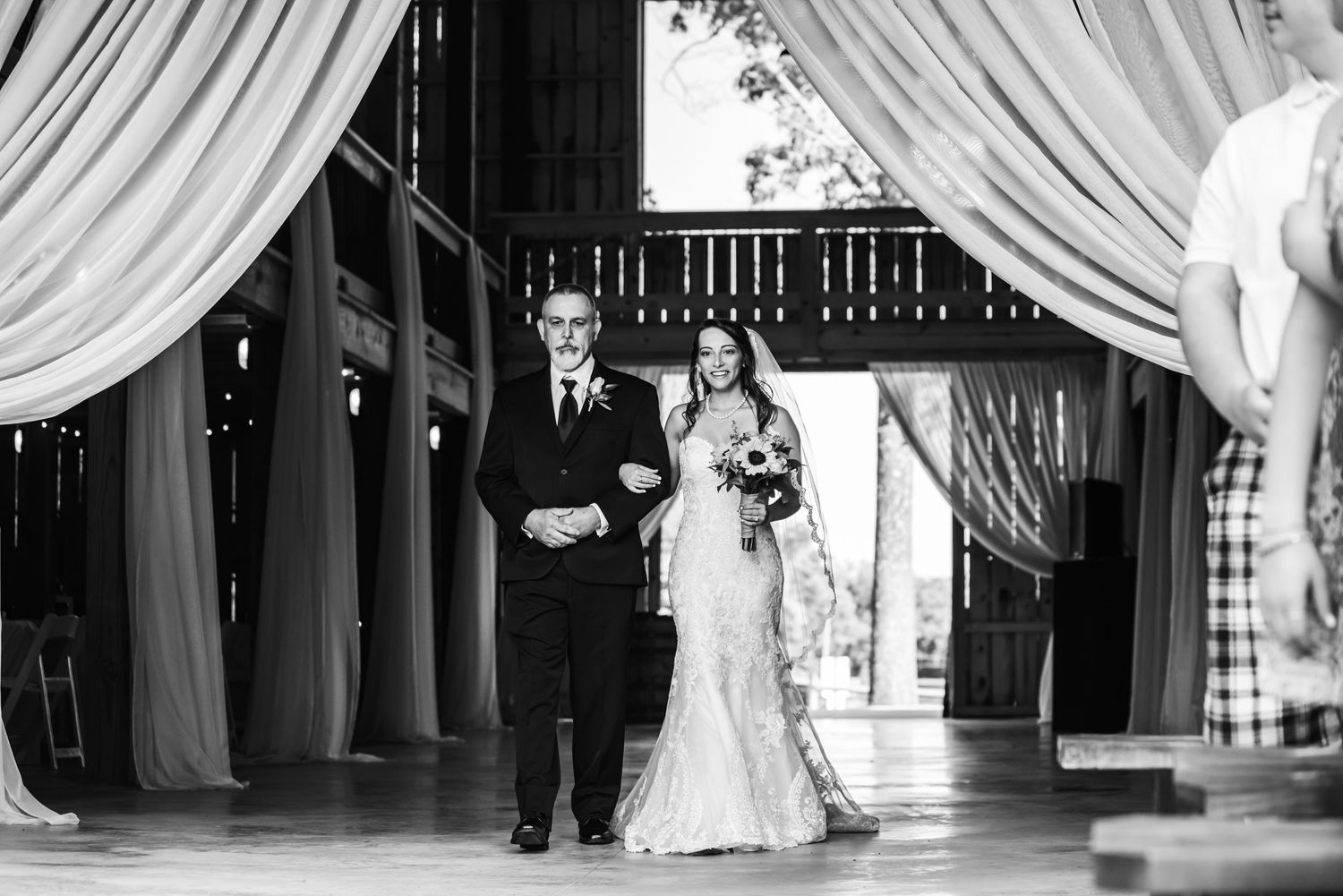 Black and white photo of bride and groom walking down the aisle at an elegant barn wedding ceremony.