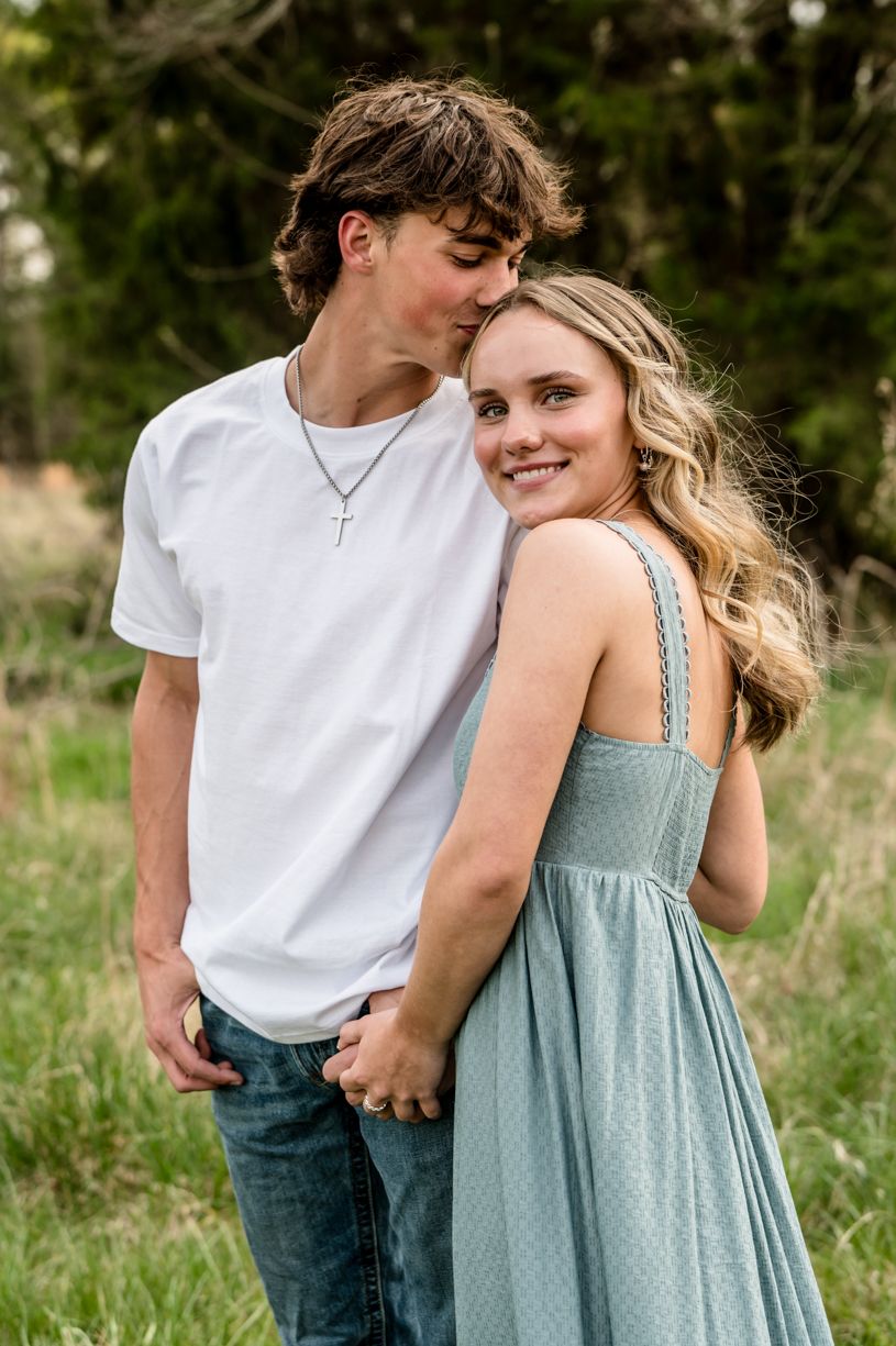 Romantic couple in casual summer outfits embracing in outdoor field setting.